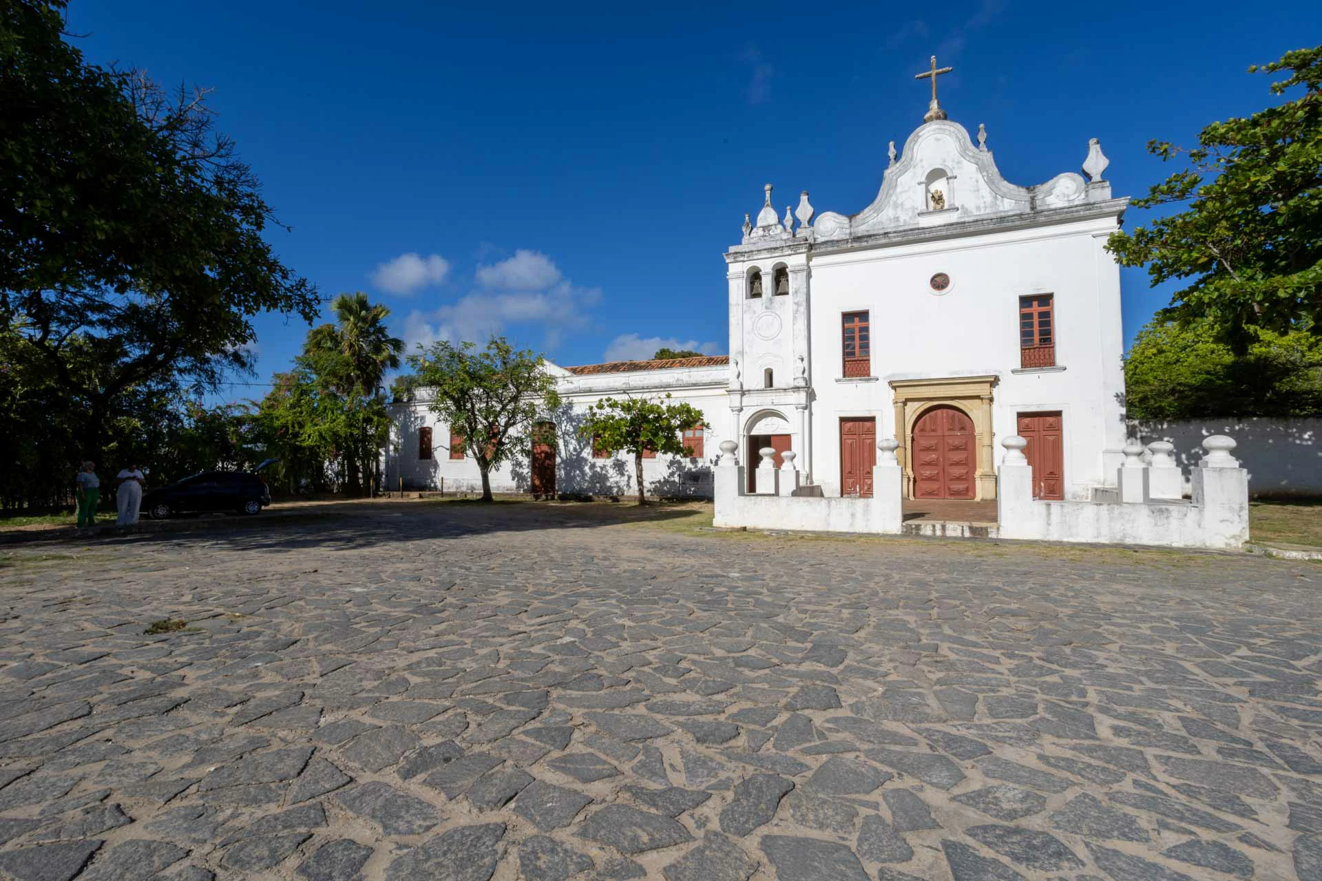 Fachada da igreja Nossa Senhora do Monte, na cor branca com portas na cor marrom, a fachada possui torre com dupla sinaleira, e com pátio na sua frente. Estilo maneirista
