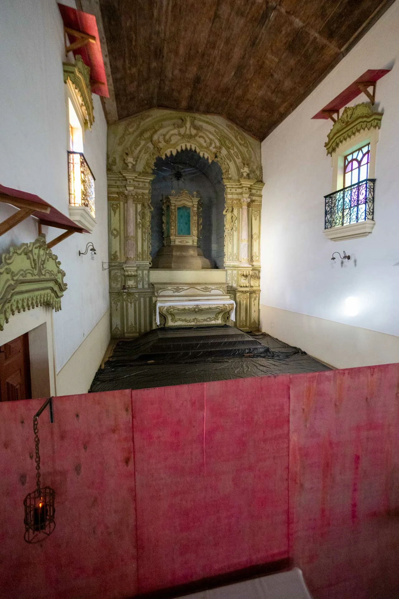 Capela-mor, teto com forro de madeira, retábulo no estilo barroco sem imagens, 1 vitral de cada parede da capela com falsa tribuna, há tapumes separando a capela da nave da igreja, e o piso está coberto com lona preta.